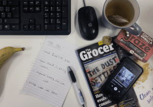 aerial shot of a desk featuring The Grocer Magazine, Twinings tea, graze protein flapjack and phone showing Oasis playing on Spotify